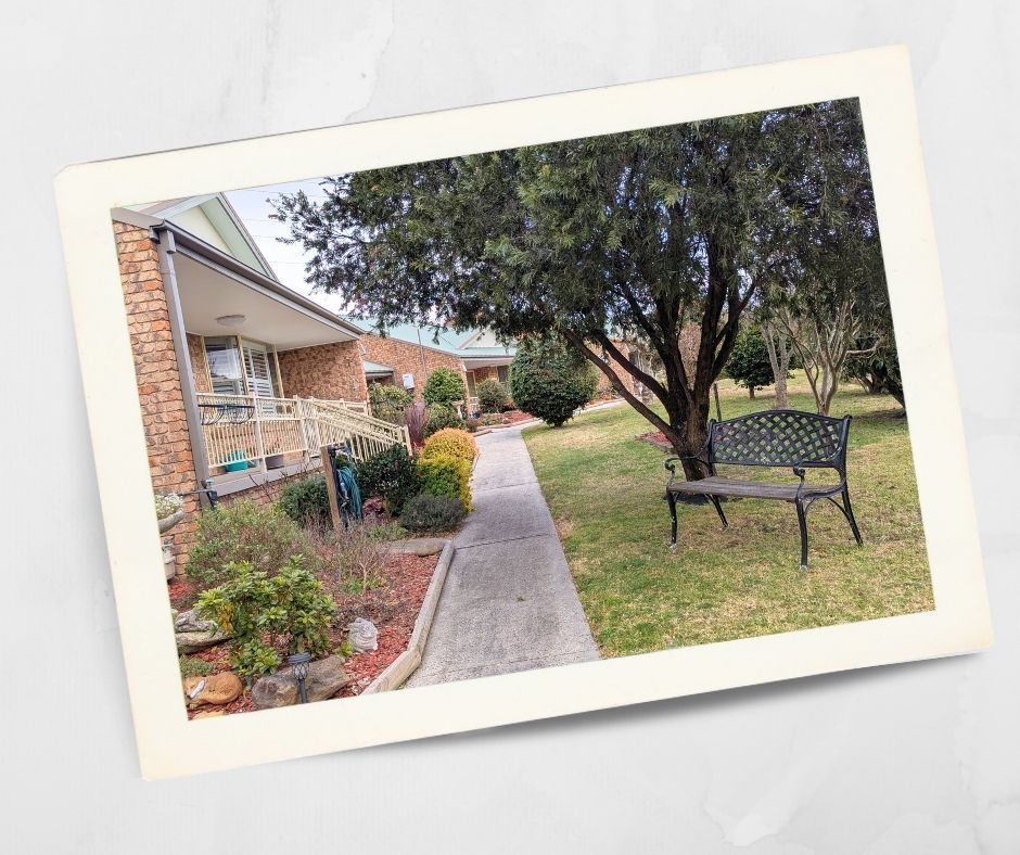 Boutique retirement village garden at Kirkley Gardens in Lithgow, featuring a tree-shaded bench, landscaped path, and brick villas with verandas.