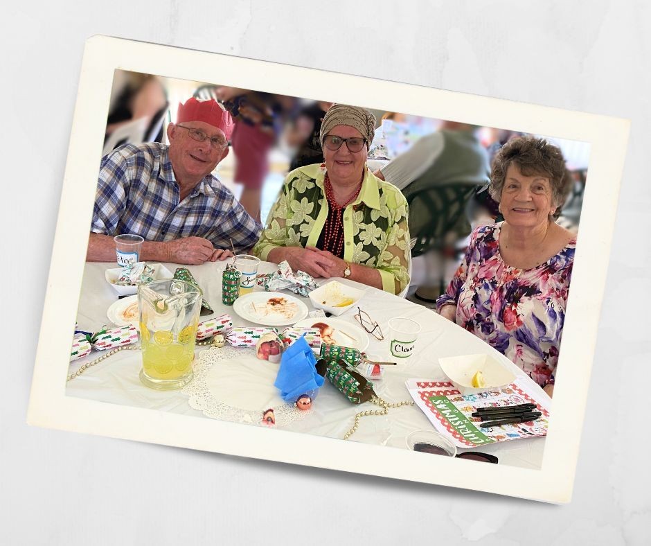 Three Kirkley Gardens residents sitting together at a Christmas lunch table, smiling and enjoying the festive gathering.