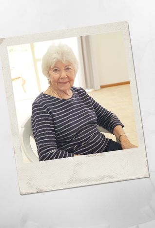 Older female resident sitting indoors at Kirkley Gardens, smiling and relaxed in a light-filled room within an independent living retirement village