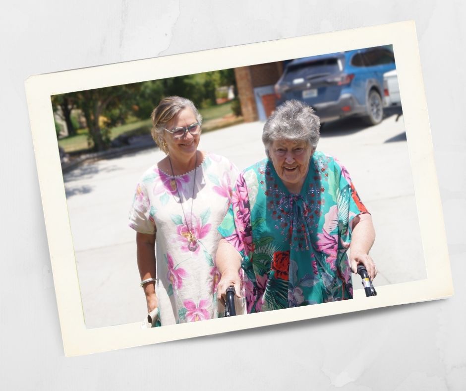 Two smiling women walking together outdoors, one using a walking frame, representing community life at a local retirement village in Lithgow.